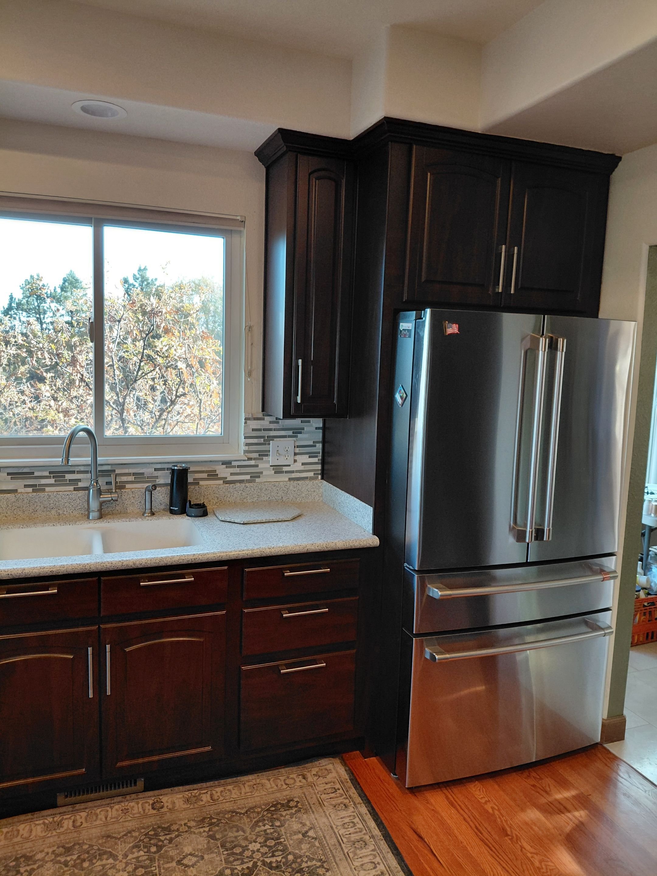 Kitchen cabinet restyle in a Colorado Springs home on Andromeda Drive featuring dark wood cabinets, updated hardware, modern backsplash, and stainless steel refrigerator