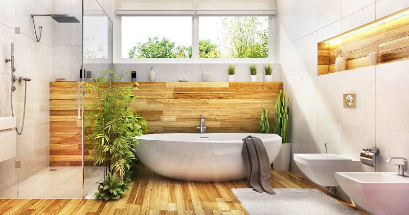 Modern biophilic bathroom with freestanding tub, natural wood accents, indoor plants, and large windows bringing in natural light.