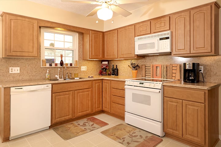 Restyled kitchen with natural wood cabinets, white appliances, and granite-look countertops after cabinet refacing