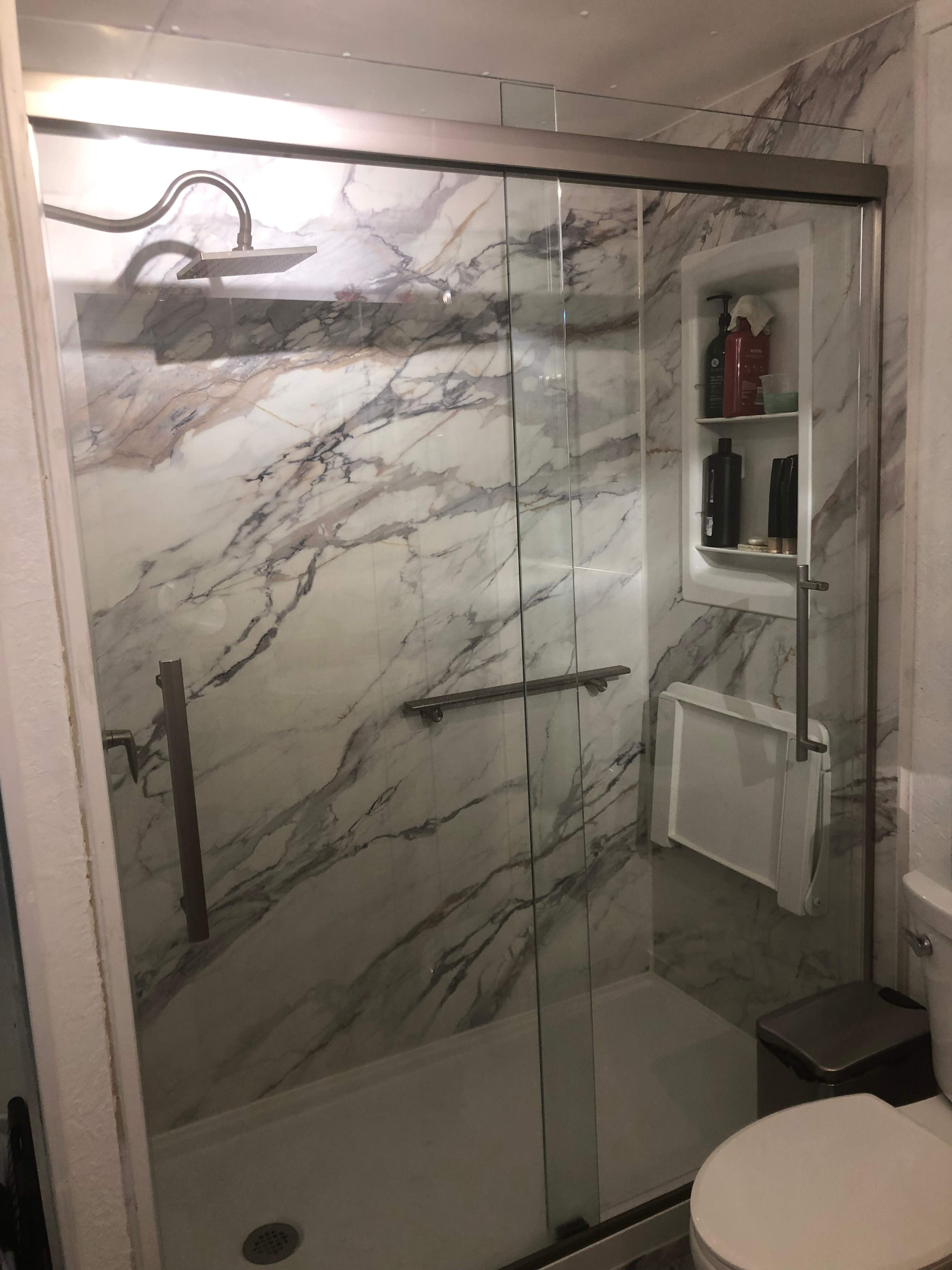 Modern shower remodel on Colorado Avenue in Grand Junction with marble-look wall panels, glass doors, built-in storage niche, and accessibility grab bars.