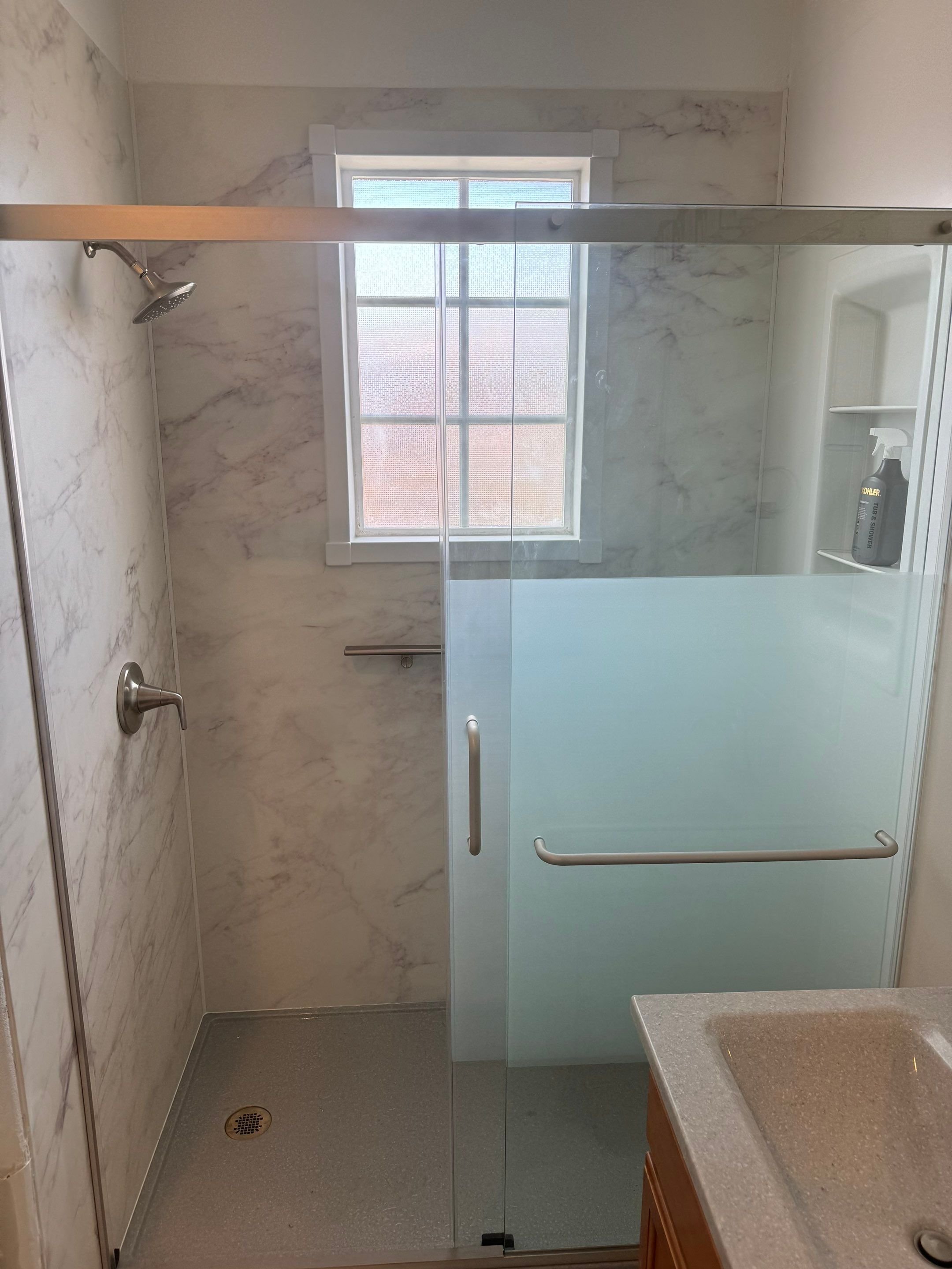 Walk-in shower remodel on E 23rd Street in Denver featuring low-threshold shower base, marble-look wall panels, glass sliding door, and grab bar for accessibility