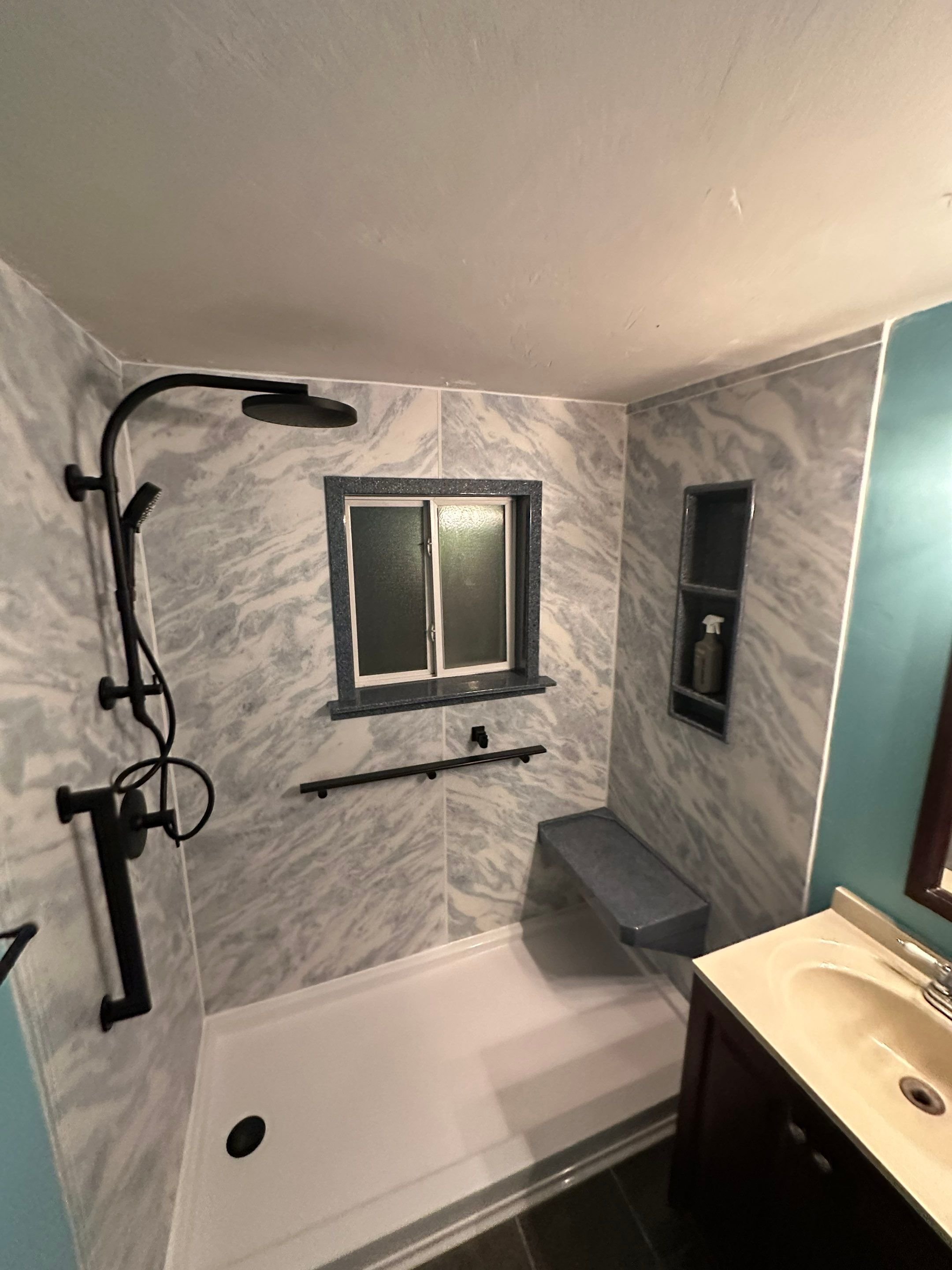 Tub-to-shower conversion in a Colorado Springs bathroom on East Monument Street with marble-look wall panels, built-in bench, and grab bar for accessibility