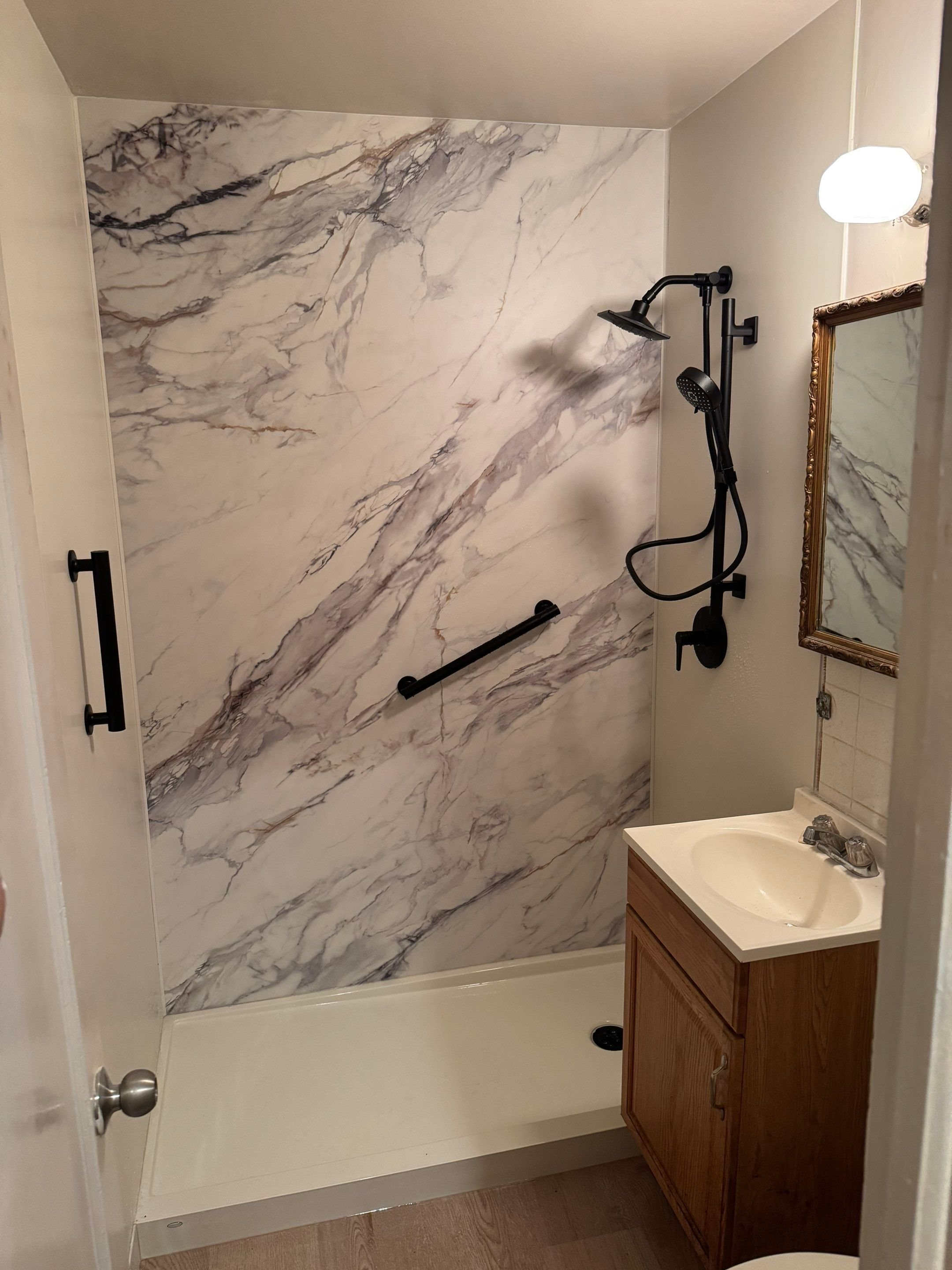 Modern walk-in shower remodel in Aurora, CO with marble-look wall panels, matte black shower fixtures, and safety grab bars