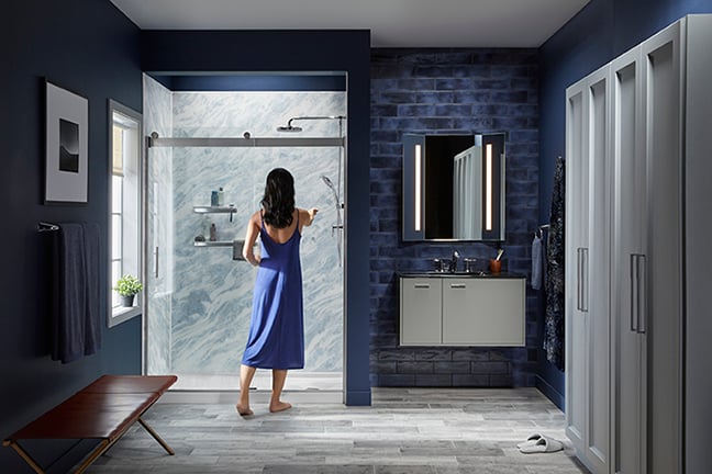 Kohler Walk-In Tub with easy-access door, handheld showerhead, and safety features, shown with senior woman entering for a safe bathing experience