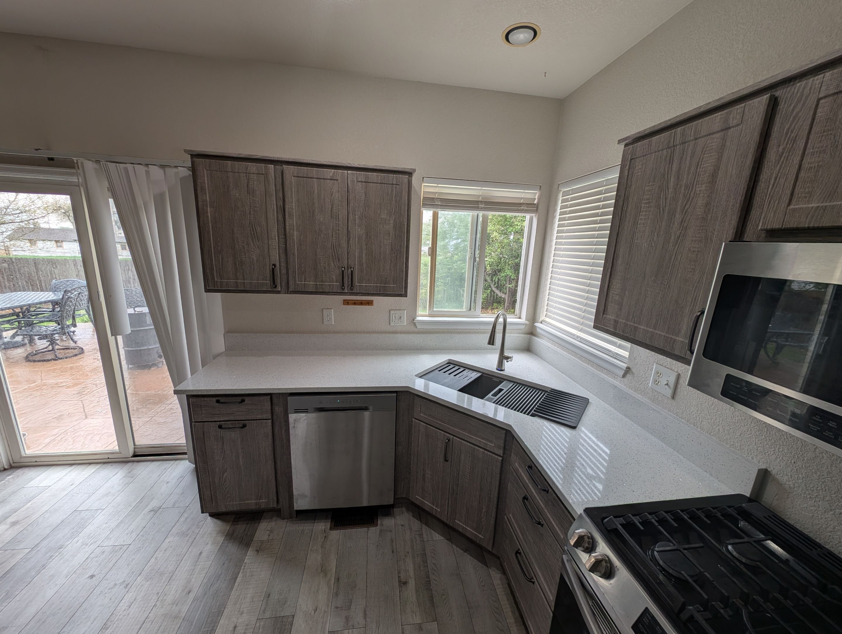 Gray woodgrain kitchen cabinet restyling in Johnstown, CO with quartz countertops, stainless steel appliances, and corner sink