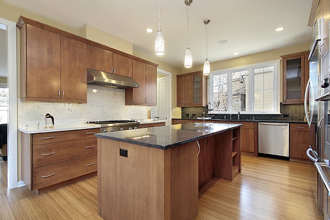 Custom kitchen cabinet restyling in Colorado Springs with warm wood cabinetry, granite countertops, and modern pendant lighting