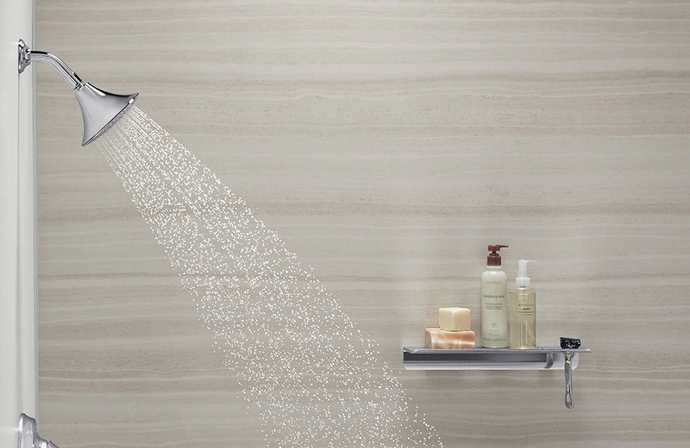 KOHLER LuxStone shower wall with brushed nickel showerhead and built-in shelf holding soap and toiletries