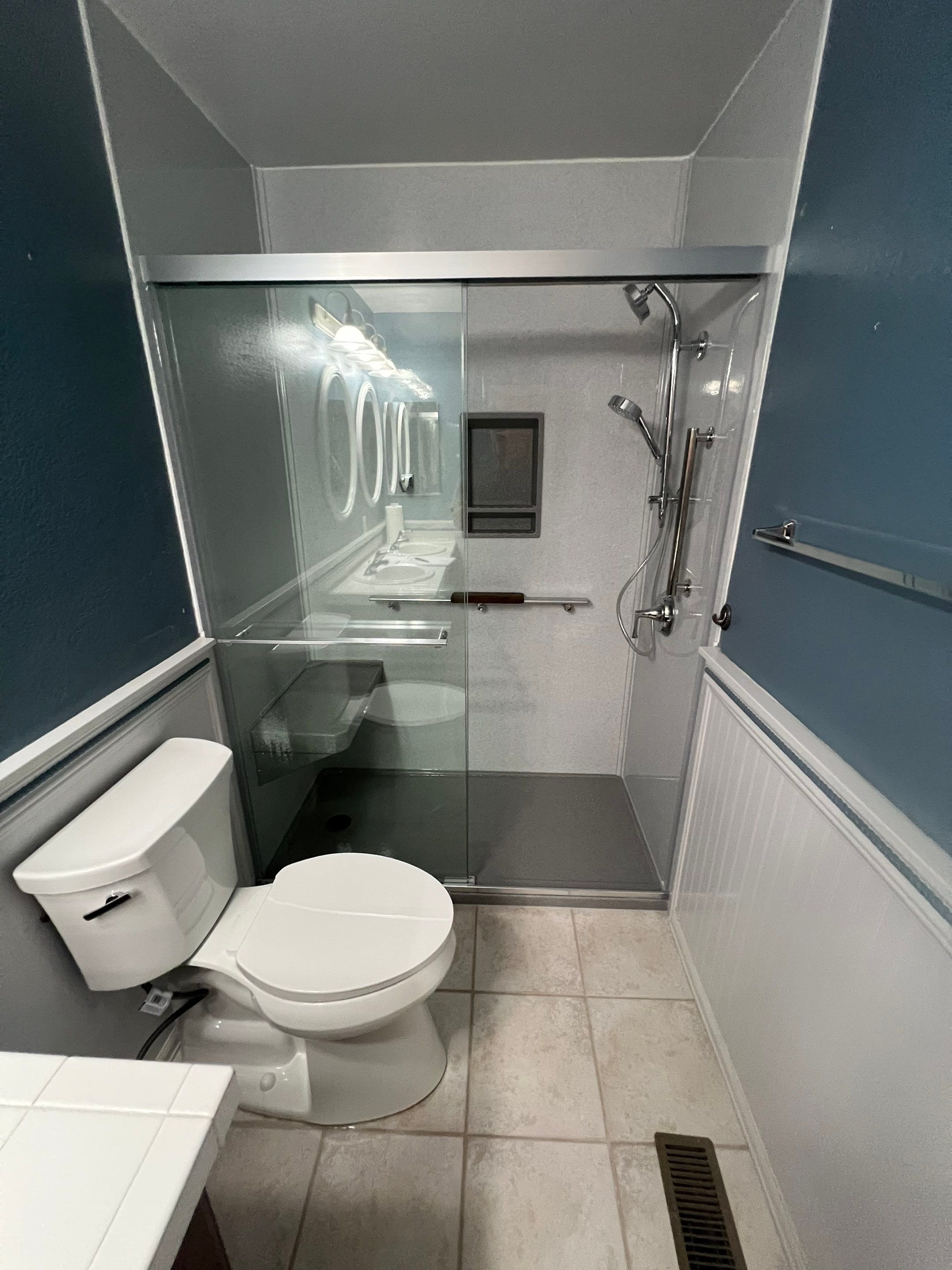 Compact Parker bathroom remodel with glass-enclosed shower and chrome showerhead above white toilet and tiled floor.