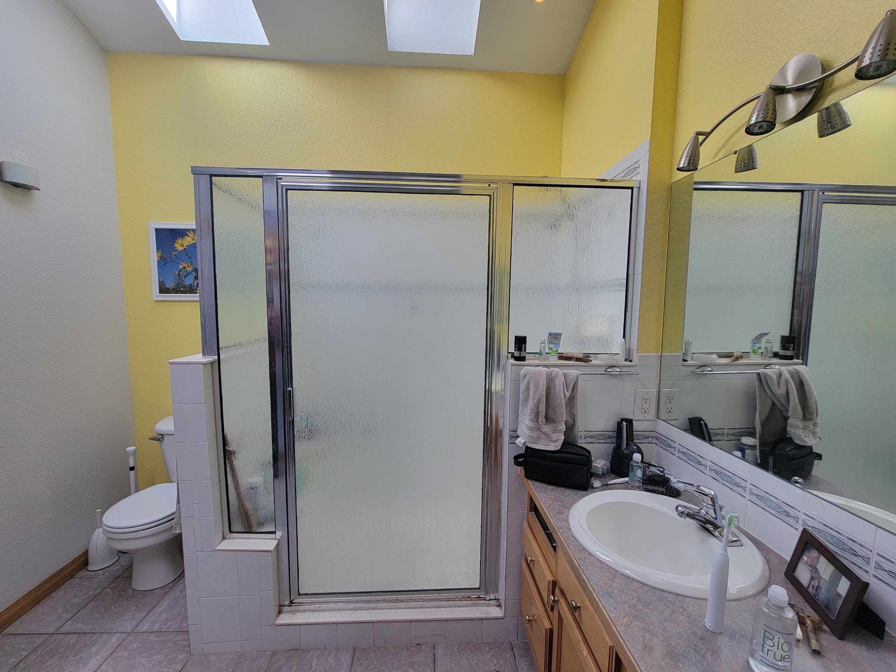 Outdated framed glass shower with yellow walls and old fixtures