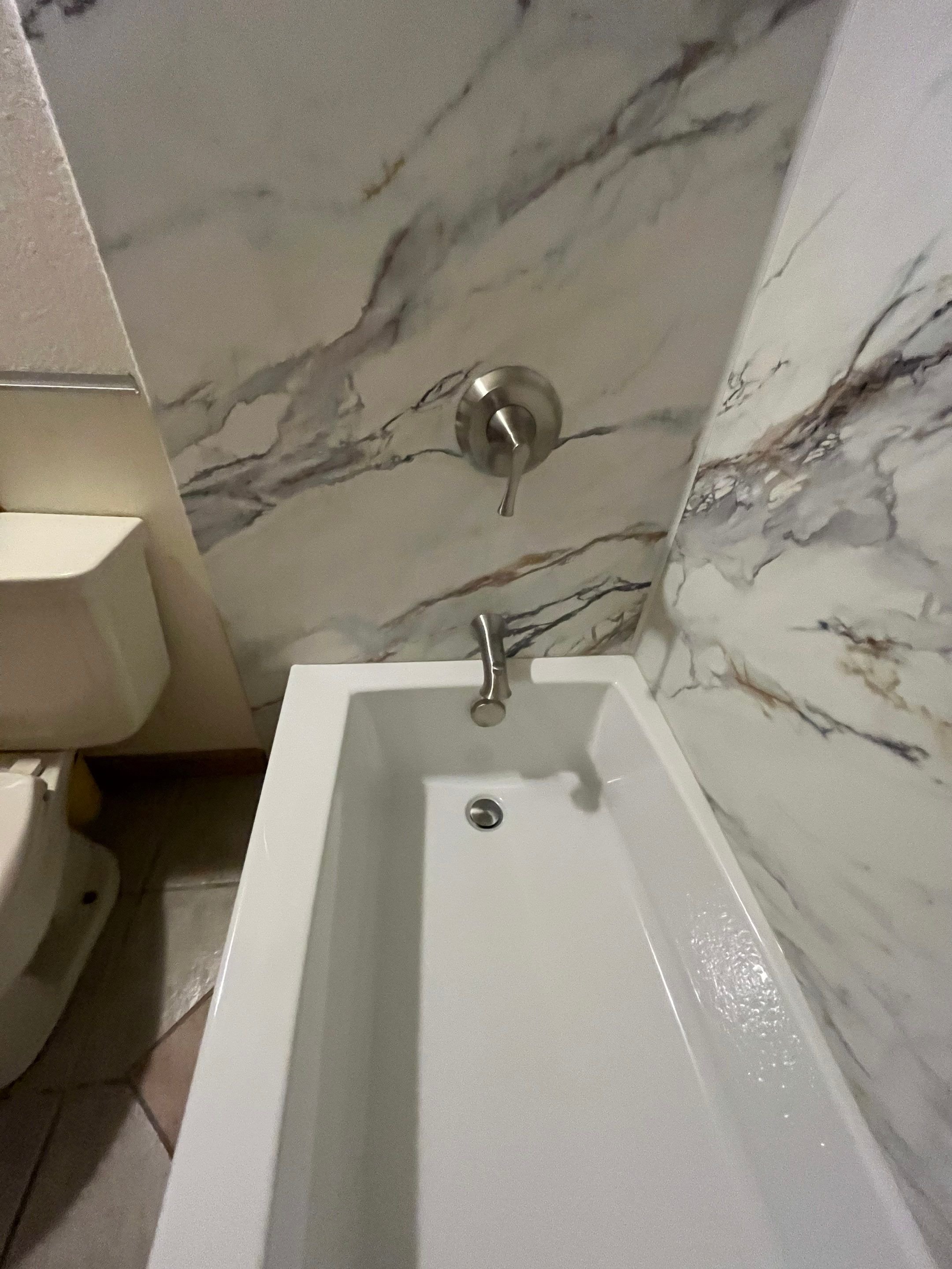 Modern rectangular soaking tub with wall-mounted faucet and marble-look wall panels in Centennial remodel.