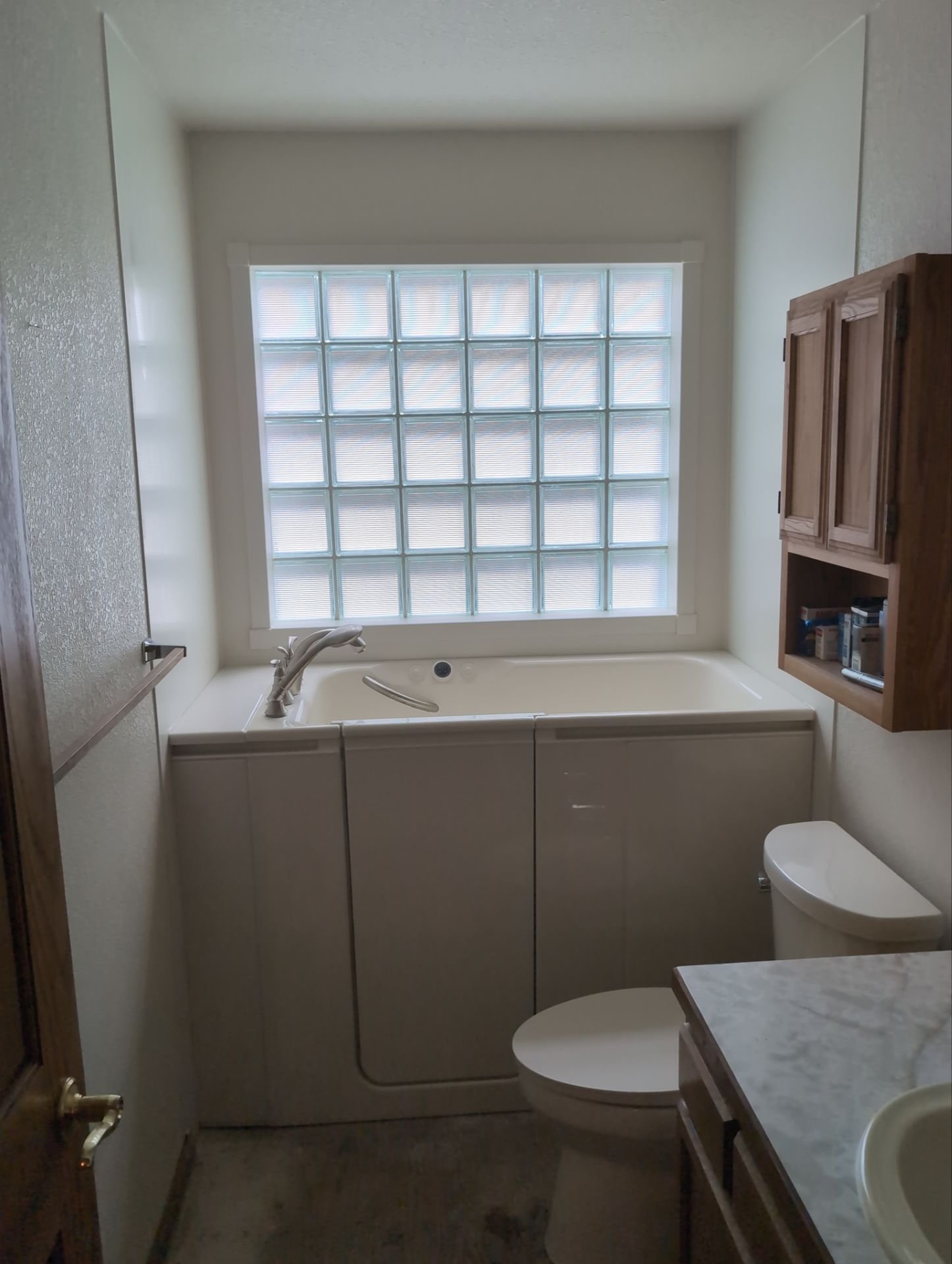 New biscuit Kohler walk-in tub installation with frosted glass block window and Kohler Cimarron toilet in a Niwot, CO bathroom remodel.