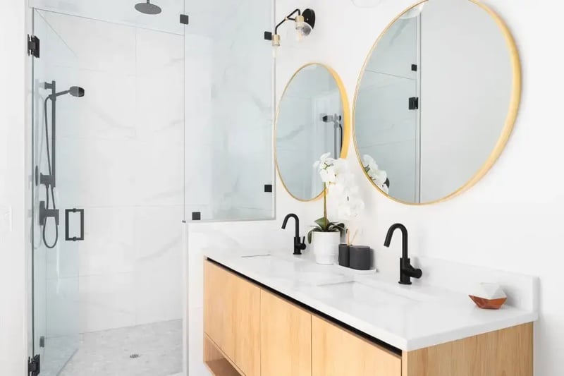 Modern midrange bathroom with wood double vanity, black fixtures, gold-framed round mirrors, and a glass-enclosed marble tile shower.