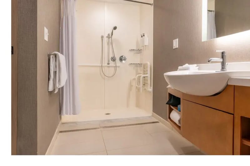 Accessible universal bathroom with roll-in shower, grab bars, fold-down shower seat, wall-mounted sink, and floating vanity.