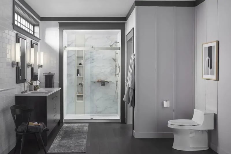 Kohler LuxStone shower with Calacatta Crema walls, featuring a sleek glass door, integrated shelving, and modern fixtures.