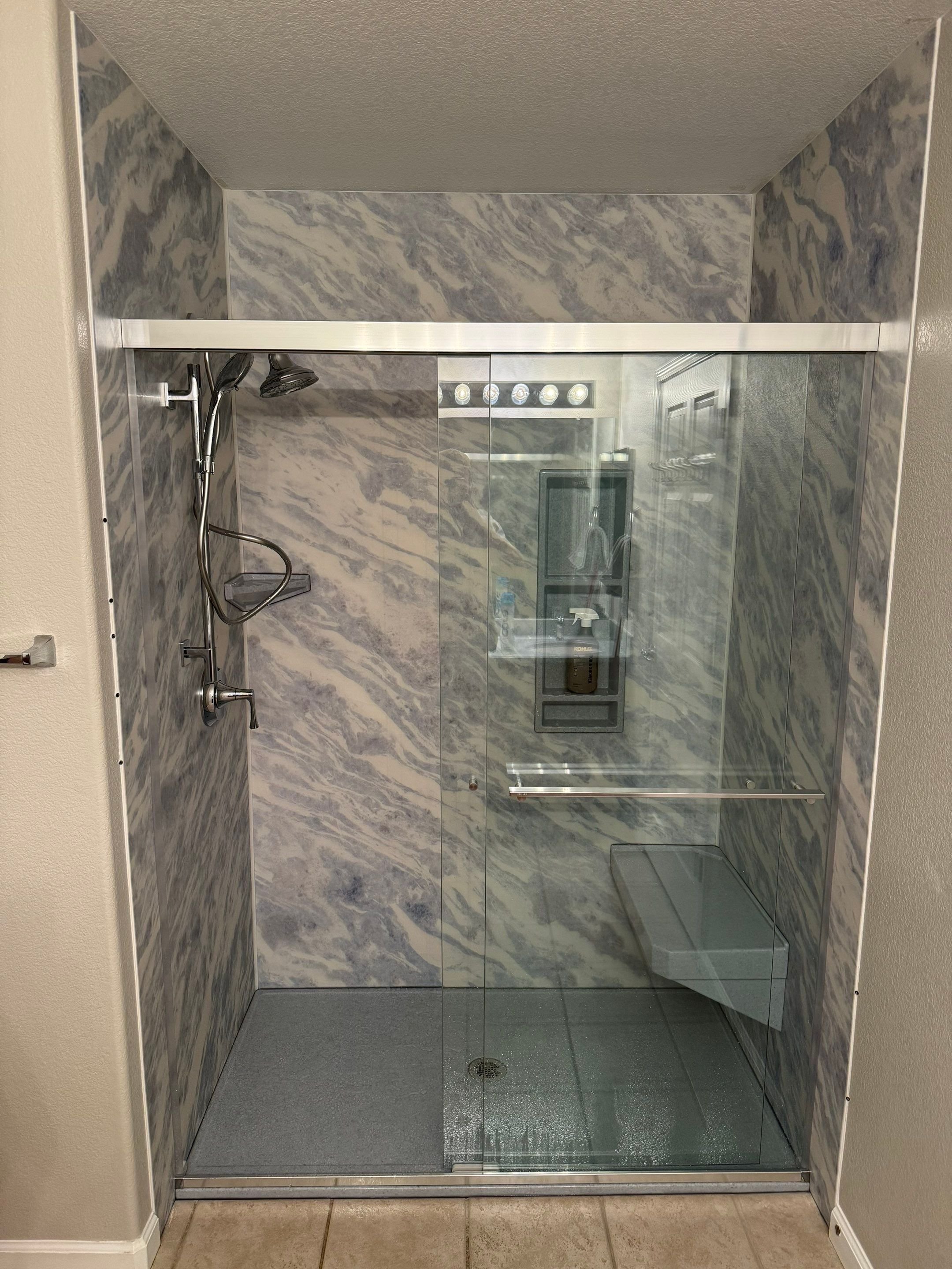Luxury walk-in shower with sliding glass door, marble-look wall panels, and built-in corner bench in Aurora, CO bathroom remodel.