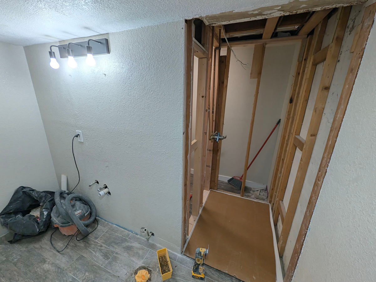 One-day shower remodel tear-out showing exposed plumbing behind the old shower