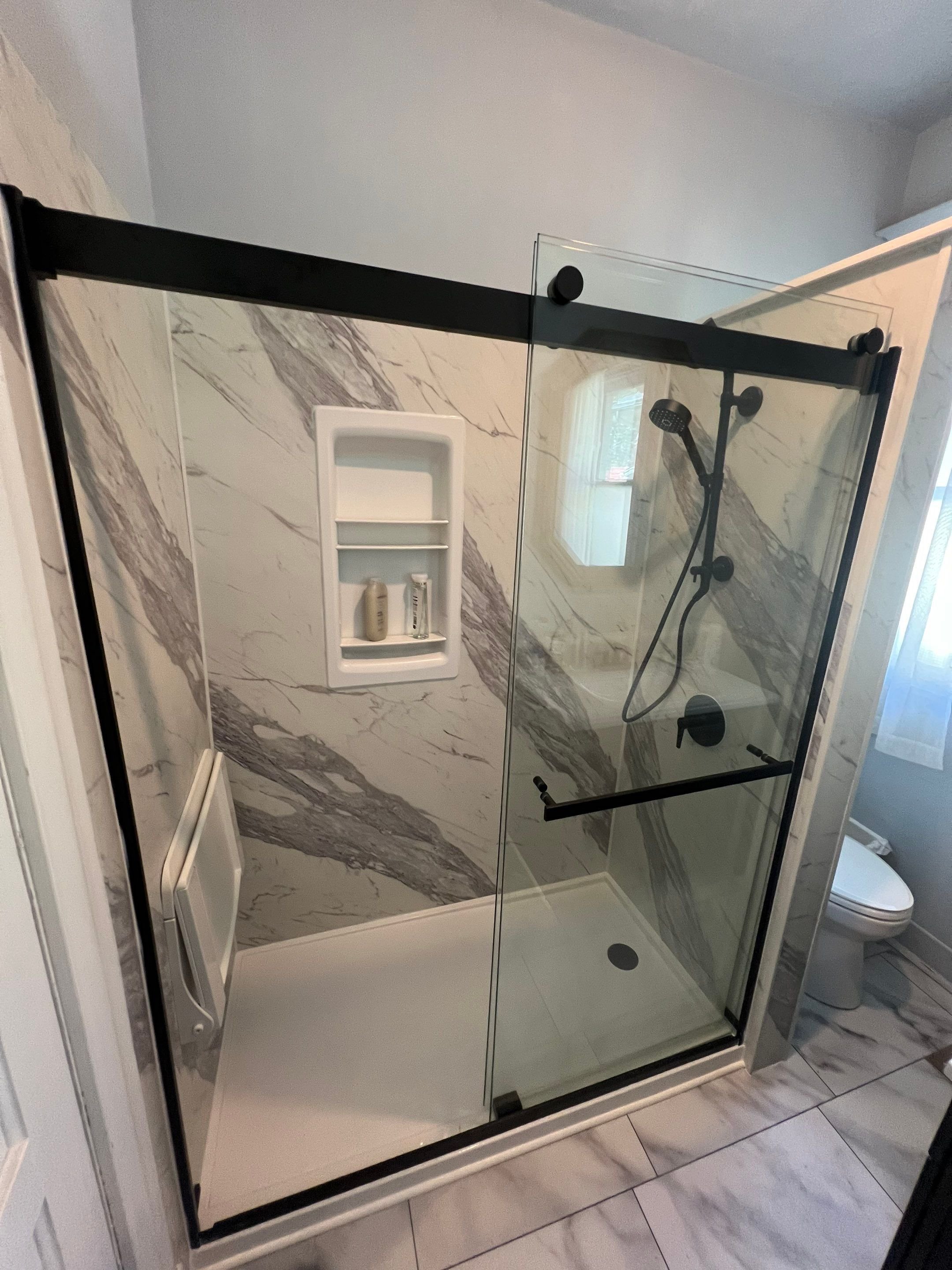 Modern walk-in shower remodel on Milwaukee Street in Denver with marble-style wall panels, black fixtures, glass enclosure, and built-in shower niche