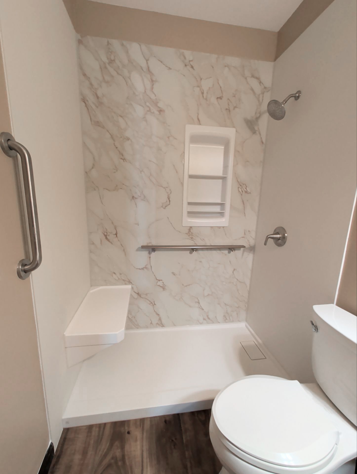 Low-threshold walk-in shower in Evergreen, CO with marble-look walls, corner seat, two grab bars, and a recessed shelf