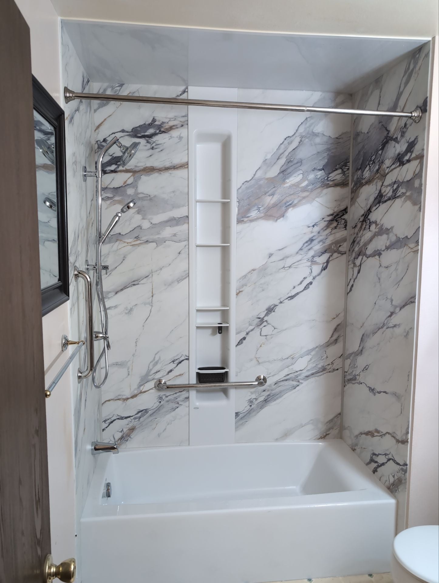 Shower-to-shower conversion in Colorado Springs featuring marble-style wall panels, a handheld showerhead, integrated storage, and safety grab bars.