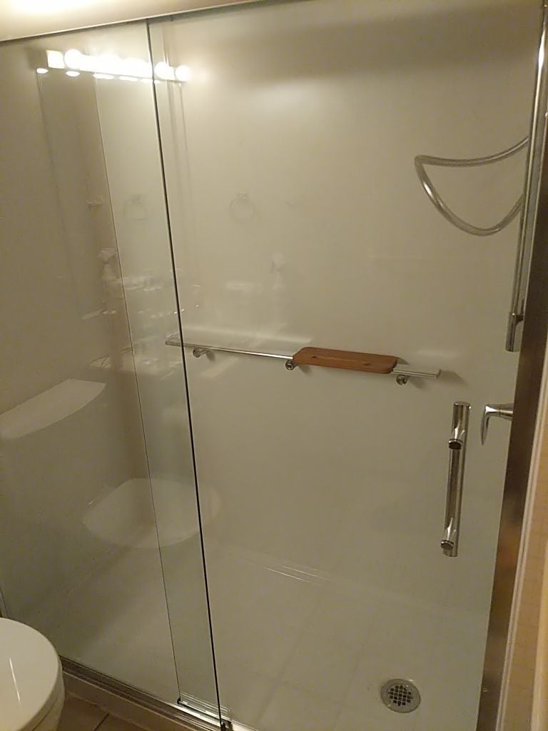 Clean white shower walls with wood-tone seat and grab bar