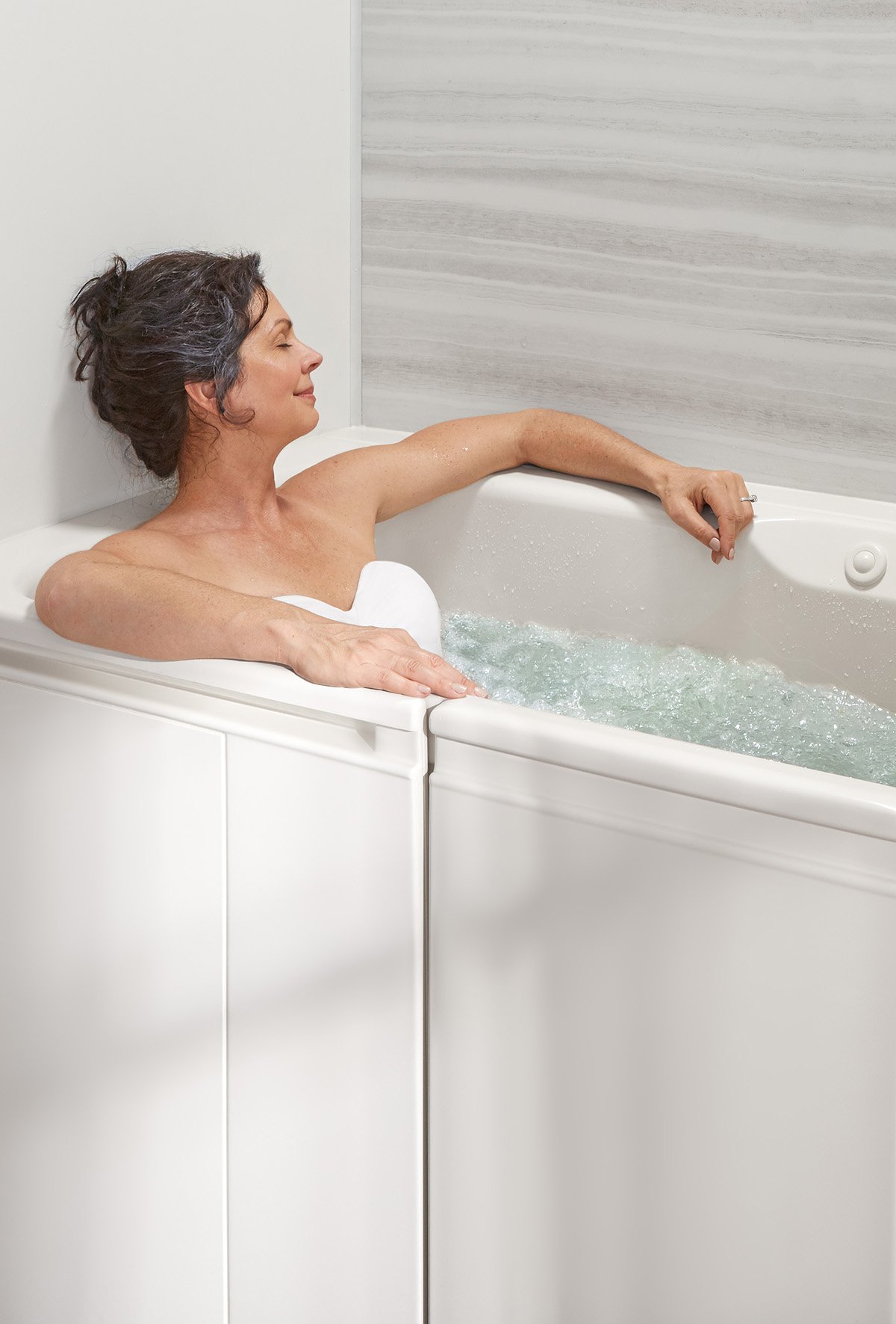 A woman relaxing in a Kohler walk-in bath with soothing whirlpool water and elegant LuxStone shower walls.