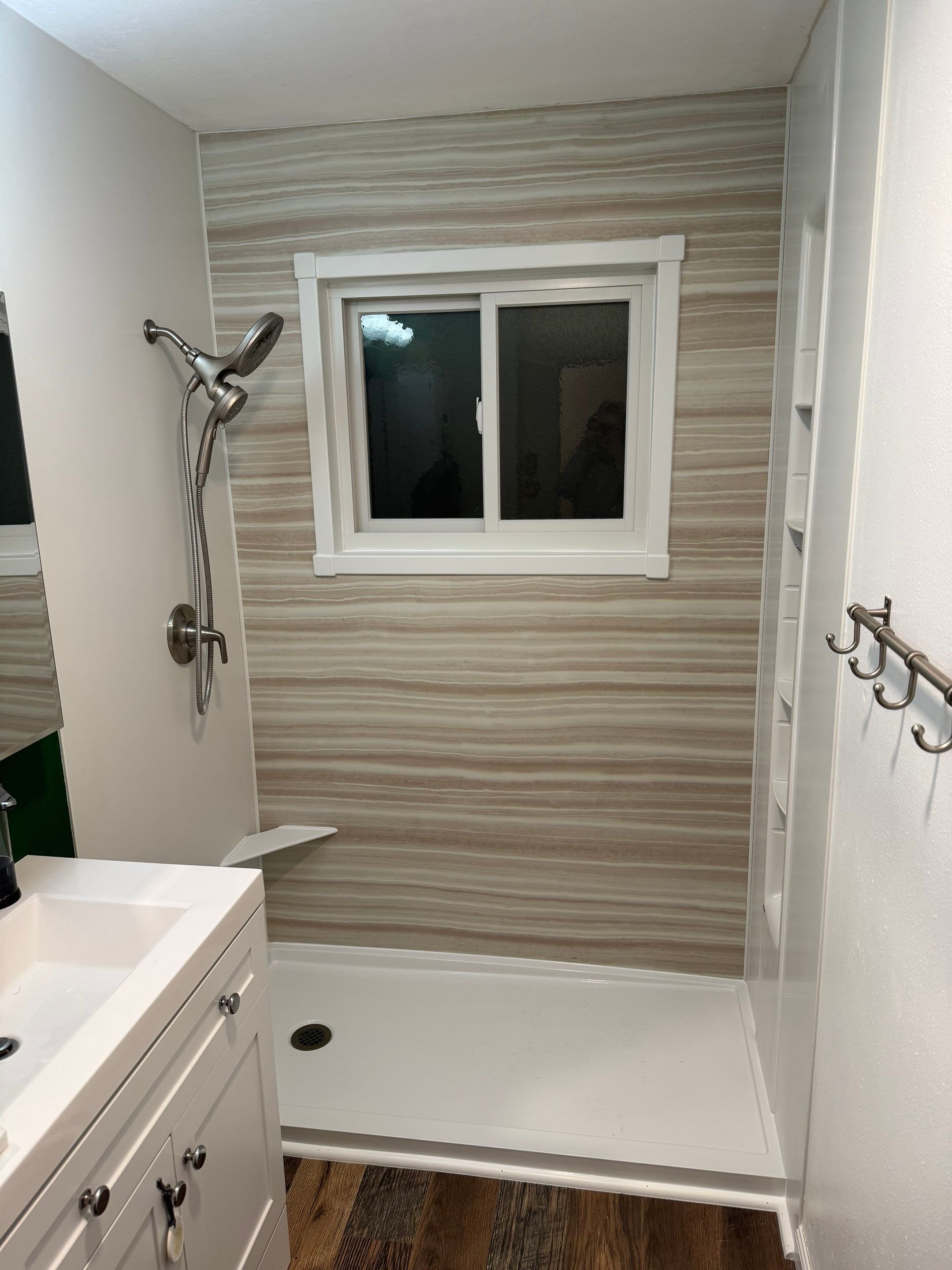 Walk-in shower remodel in Aurora, CO featuring horizontal striated wall panels, updated window trim, and handheld showerhead